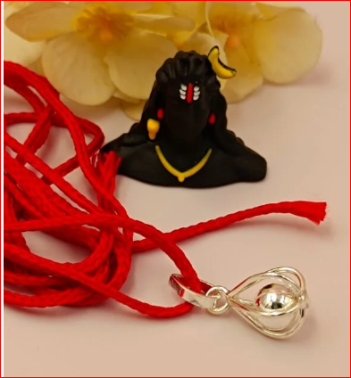 Black figurine with red string and gold pendant on a light background