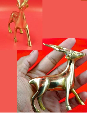Gold deer figurine held in a hand against a red background