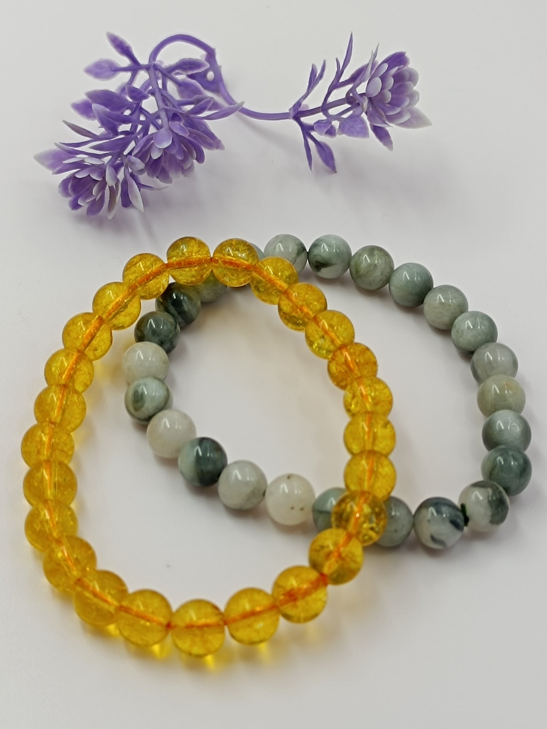 Two beaded bracelets, one yellow and one multicolored, with purple flowers on a white background.