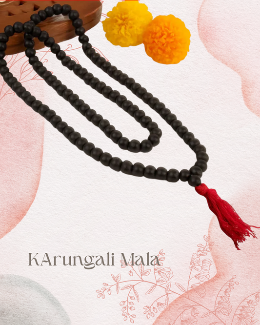 Black beaded mala necklace with a red tassel on a light pink floral background, featuring the brand 'KArungali Mala'.